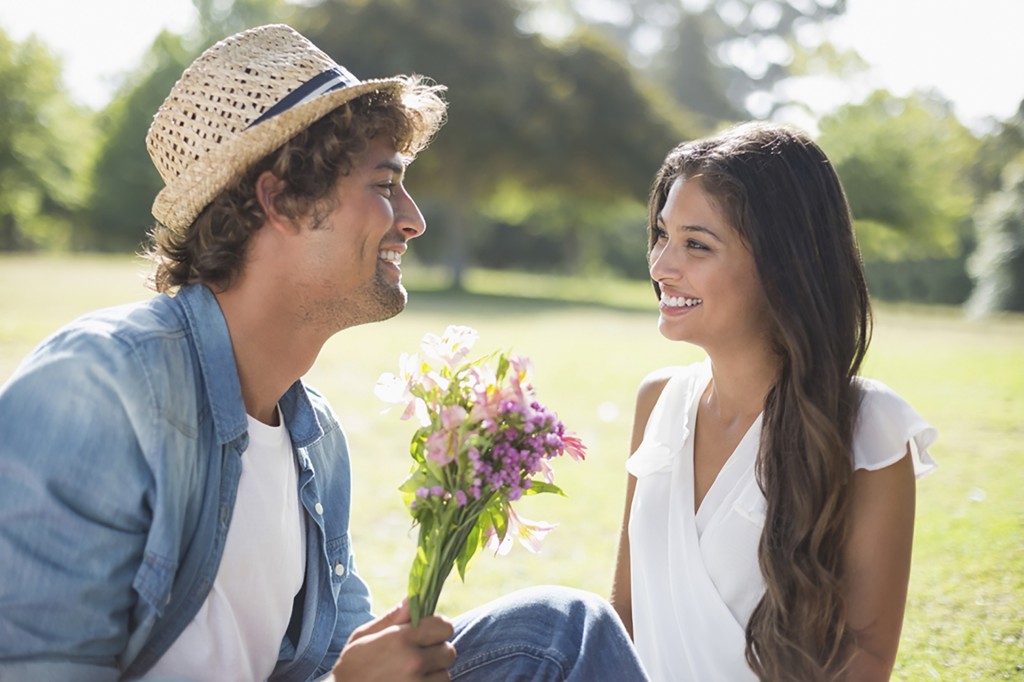 Young man offering his girlfriend purple flowers in the park on a sunny day